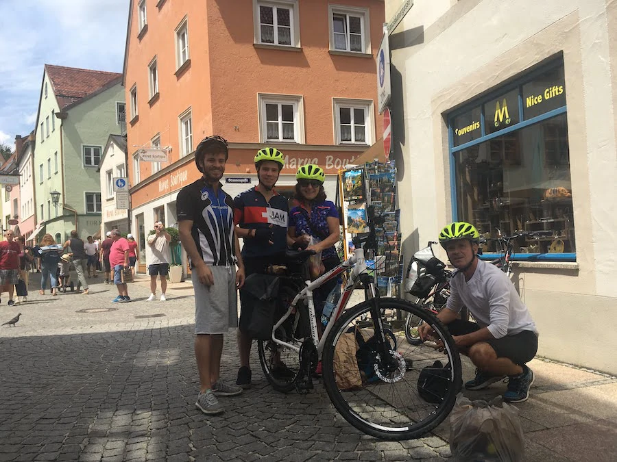 Scenic cycling journey from Salzburg to Grado: a group of cyclists enjoying a vibrant European town square with colorful buildings and a souvenir shop