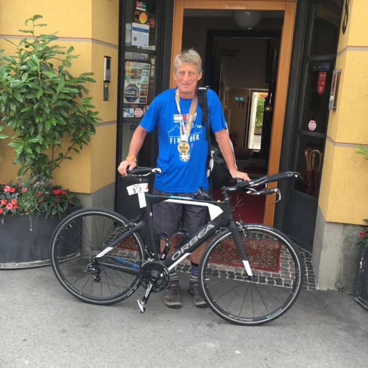 an athlete with medal is on the door of a hotel and is leaning on the TT bike rented for the ironman race